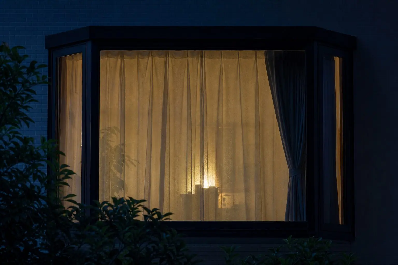 夜に屋外から見た出窓のレースカーテン越しの室内